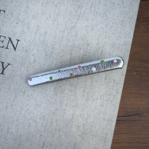 Vue détaillée d'une barrette argentée à pois colorés posée sur un tissu gris