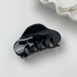 Détail d'une pince à cheveux noire minimaliste en acétate sur un plateau décoratif