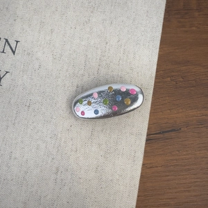 Gros plan sur une pince à cheveux argentée avec des pois colorés sur fond de lin