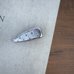 Détail d'une pince à cheveux argentée avec des points colorés et texture martelée sur lin