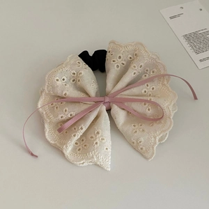 Detail of a creamy lace bow hair tie with pink ribbon and floral embroidery patterns