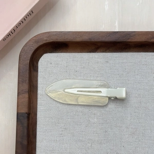 Dettaglio di un fermaglio per capelli bianco crema con glitter su vassoio in legno