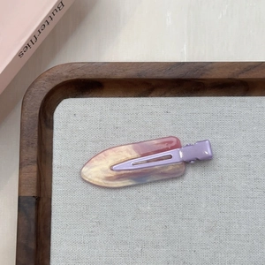 Dettaglio del fermaglio per capelli in resina marmorizzata viola su vassoio di legno