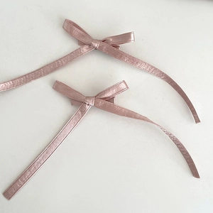 Détail de deux barrettes à nœuds en satin rose avec de longs rubans fluides style ballet