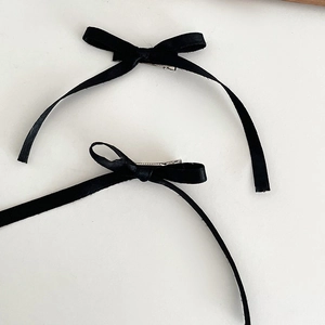 Détail de deux barrettes à nœuds en satin noir avec de longs rubans et des pinces crocodiles en métal