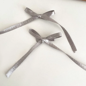 Détail de deux barrettes nœuds argentés avec longs rubans sur fond blanc épuré