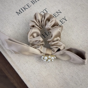 Detail of champagne satin scrunchie featuring elegant ribbon bow and white faux pearl clusters