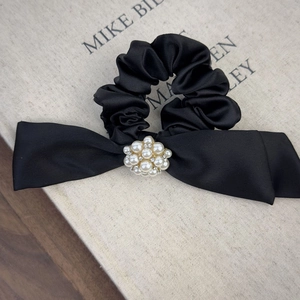 Detail of black satin scrunchie with crystal floral center and elegant bow design