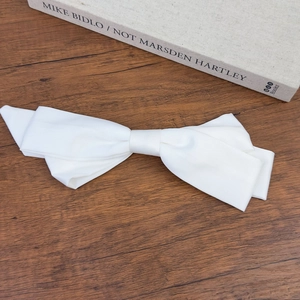 Detailed view of a white satin bow hair clip on a vintage book and wooden desk