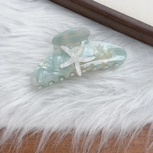 Detailed view of mint green acetate hair claw clip featuring starfish and star patterns