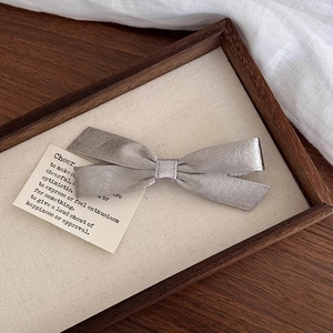 Detailed view of elegant silver grey satin bow hair clip on a wooden display tray