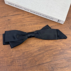 Detailed view of a large black satin bow hair clip on a wooden background with art books