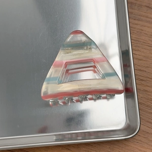 Detail of a triangle hair claw clip with colorful acetate stripes on a metal tray