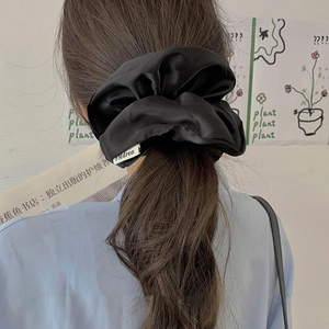 Close-up of a black oversized satin scrunchie on a ponytail with a silky texture