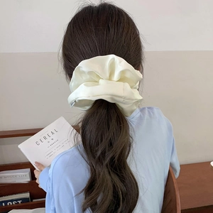 Elegant oversized cream satin scrunchie with glossy pleated texture worn on long hair