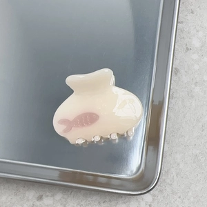 Vue détaillée d'une pince à cheveux crème avec motif de poisson rose sur un plateau argenté
