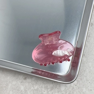 Gros plan d'une pince à cheveux rose avec motif de poisson sur un plateau en métal