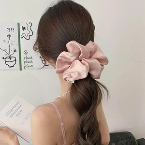 Detailed view of a soft pink satin scrunchie styled on a brunette low ponytail