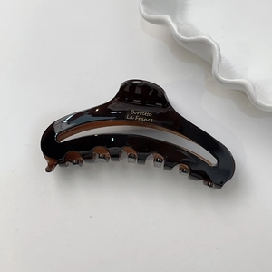 Détail de la pince à cheveux en acétate marron foncé avec inscription dorée sur blanc