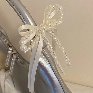 Barrette élégante avec nœud en perles blanches et ruban de satin sur un sac argenté