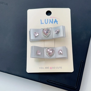 Détail de barrettes nœuds en satin argenté avec strass cœur rose sur carte blanche