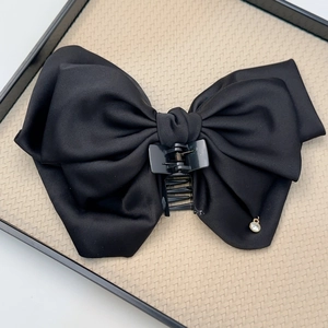 Detail of a large black satin bow hair claw clip with a delicate rhinestone pendant