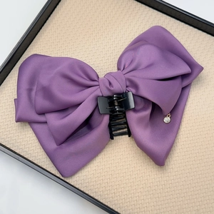 Detail of a purple satin bow hair claw clip with a sparkling rhinestone pendant