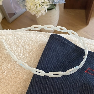 Détail d'un serre-tête en acétate blanc avec dents antidérapantes sur un tissu texturé