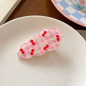Detail shot of a pink checkered hair clip with red cherry prints on a white dish