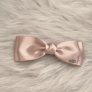 Detail of the pink satin bow hair clip with layered fabric and silver brand plate