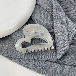 Détail d'une pince à cheveux en forme de cœur marbré sur tissu gris et fond en céramique