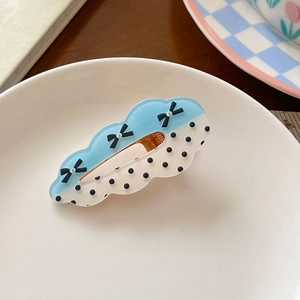 Detail of cloud-shaped hair clip with blue acrylic, black bows, and polka dots on white plate