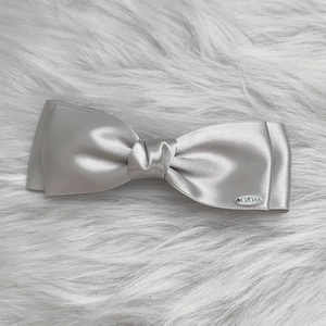 Detail shot of a silver grey satin bow hair clip with an oval metal brand tag