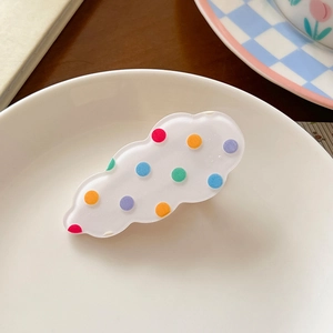 Detail shot of a cloud-shaped acrylic hair clip with colorful polka dots on a white tray