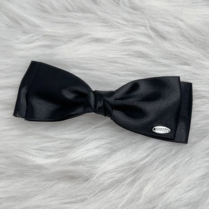 Detail of the high-quality black satin bow hair clip with an oval silver metal logo tag