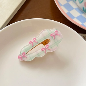 Detail of cloud-shaped hair clip with pink bows and green plaid pattern on ceramic plate