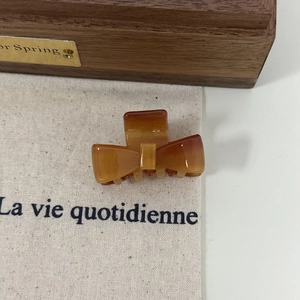 Close-up of amber acetate bow hair claw clip with golden label on wooden background