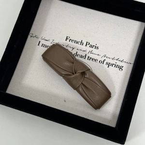 Close-up of brown PU leather knotted hair clip with retro grain texture on canvas tray