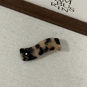 Détail d'une pince à cheveux ondulée en acétate avec motif écaille noir et blanc et logo doré