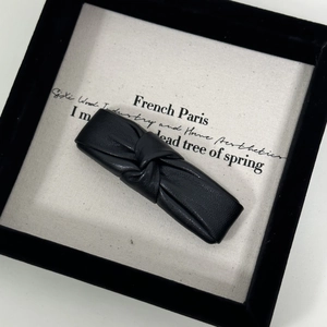 Close-up of black PU leather knotted hair clip resting in a premium jewelry gift box