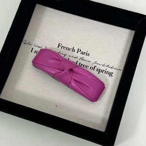 Close-up of fuchsia PU leather knotted hair clip with elegant textured bow on canvas
