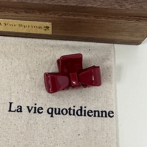 Close-up of a burgundy acetate bow hair claw clip on a rustic textured background