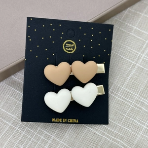 Vue détaillée de deux pinces à cheveux coeur mat en kaki et crème sur carte de support