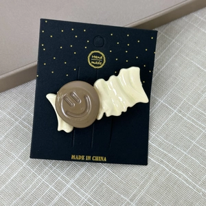 Détail d'une pince à cheveux avec motif smiley marron et crème sur carte de support