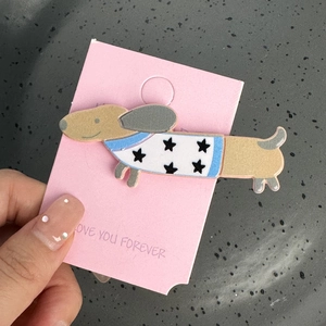 Détail d'une pince à cheveux teckel en acrylique avec étoiles sur support rose tendre