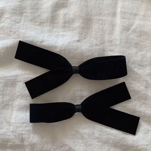 Elegant pair of black velvet bow hair clips with long ribbons on white linen fabric