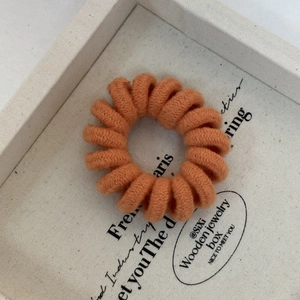 Detailed macro view of orange knit-wrapped spiral telephone wire hair tie on a jewelry box