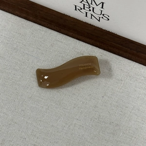 Détail de la pince à cheveux ondulée en acétate marron avec lettrage doré