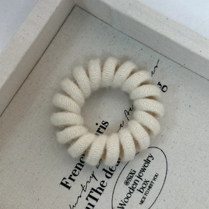 Close-up of beige knitted spiral telephone wire hair tie showing soft wool texture