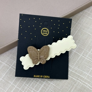 Détail d'une pince à cheveux papillon en résine marron et beige sur carte artisanale